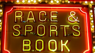 Bright neon lights on a marquee sign display the words 'RACE & SPORTS BOOK'. The sign is surrounded by rows of yellow and white lights against a red background, evoking a vibrant, energetic atmosphere typically associated with casinos or entertainment venues.