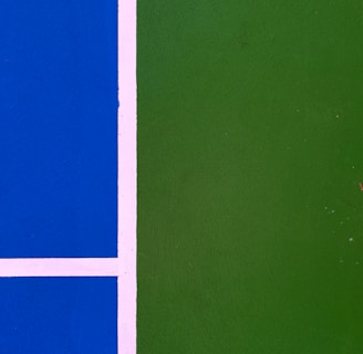 A close-up view of a sports court with a bright blue section on the left and a green section on the right, separated by white lines.