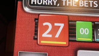 A digital display screen showing a casino betting interface, with text prompting to hurry bets and a highlighted number 27 in red. There are options for betting amounts and a 'share bets' button.