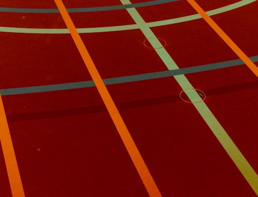 A sports court with intersecting lines in orange and blue, creating geometric patterns on a reddish-brown surface.