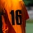 A person is wearing an orange sports jersey with the number 16 printed in black on the back. The background is blurred, but it appears to be an outdoor environment, possibly a sports field.